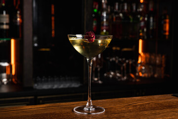 An alcoholic cocktail served in a coupe glass garnished with rose on a wooden bar counter