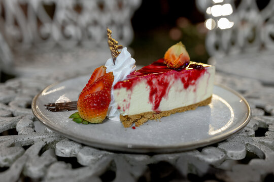 cheesecake frutos rojos, con un emplatado de alta cocina, en una silla antigua de color blanco.
