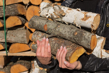 Female hands hold a bundle of firewood, against the background of a pile of firewood stacked on a pallet