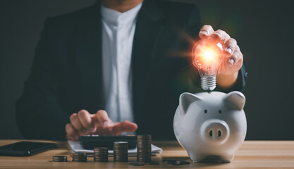 Businessman holding lightbulb  on piggy bank and pressing calculator, financial accounting, saving...