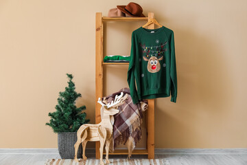 Shelving unit with sweater, wooden reindeer and Christmas tree near beige wall