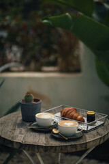 Two cups of cappuccino and fresh croissant with jam on wooden table.