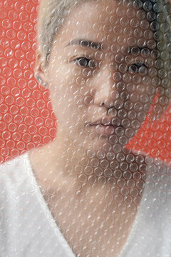 Close up portrait of young female model behind plastic bubble wrap against red background