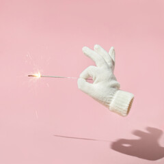 Christmas winter creative layout with mitten holding sprinkler on pastel pink background. 80s or 90s retro aesthetic holiday concept. Minimal season idea.