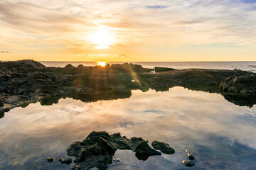 beautiful sea sunrise on a rocky sea coast with calm water , amazing cloudy sky and reflection on water surface