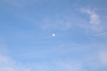 Beautiful blue sky and fluffy cloud landscape background. Moon during the day, full face of the Moon reflecting sunlight. 