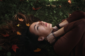 Portrait of sad beautiful young woman lying on the ground of an autumn forest with colorful maple...