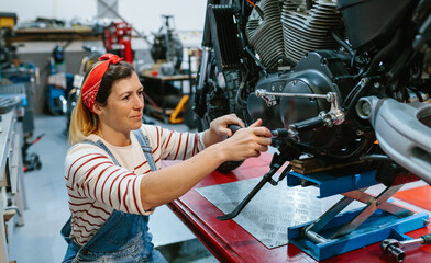 Portrait of happy mechanic woman with tool reviewing engine of custom motorcycle over platform on...