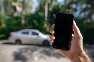 Smartphone mockup in hand against the background of a street and a car in summer. Car rental or car...