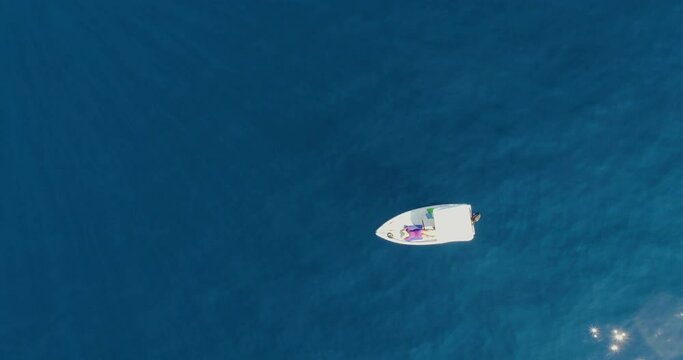 Aerial drone top shot over small white Boat Boat in the middle of the sea with young woman in purple lying on a sunny day