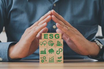 Hand holds wooden cubes with abbreviation ESG standing with other ESG icons on grey background. ESG...