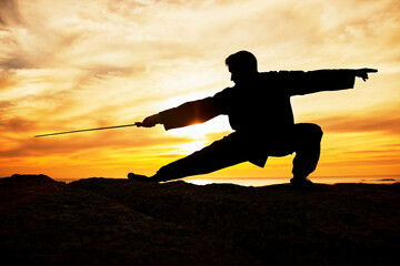 Sunset, sport and man doing tai chi with a sword on a hill for exercise and fitness workout....