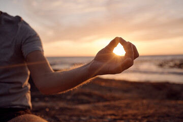 Beach meditation, sunset and hands of man meditate for peace, freedom and chakra energy healing of soul aura. Sun flare, lotus and spiritual yogi relax at ocean sea for zen mindset and mindfulness