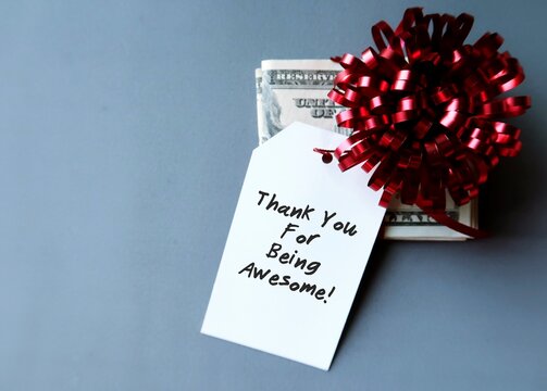 Cash Dollars Money On Gray Background With Red Gift Bow And Tag Written THANK YOU FOR BEING AWESOME! - Concept Of Year End Gift Money Or Bonus For Employee Or Team Staff To Express Appreciation  