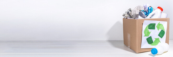 Garbage sorting, waste recycling concept. Box with recycling materials - plastic, glass, paper, cardboard, on white wooden background copy space. Woman hands sorting various rubbish and trash