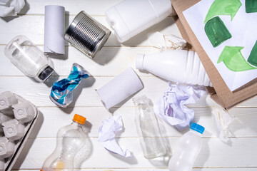 Garbage sorting, waste recycling concept. Box with recycling materials - plastic, glass, paper, cardboard, on white wooden background copy space. Woman hands sorting various rubbish and trash