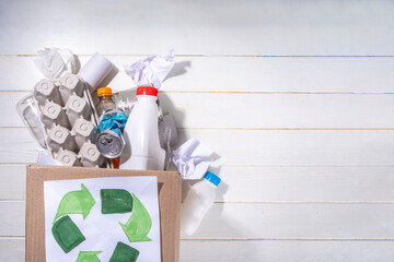 Garbage sorting, waste recycling concept. Box with recycling materials - plastic, glass, paper, cardboard, on white wooden background copy space. Woman hands sorting various rubbish and trash
