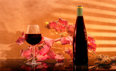 Verre de vin rouge avec une bouteille de vin sans étiquette avec en arrière plan des feuilles de vignes avec rayons du soleil à travers des persiennes. 