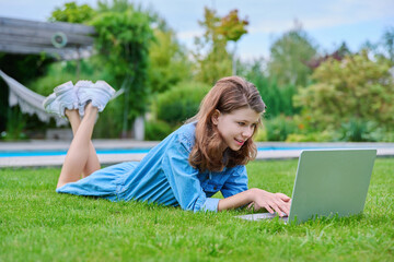 Preteen girl lying on grass in backyard using laptop for relaxing and studying