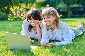 Fototapeta premium Teenage female student friends laughing lying on grass with laptop