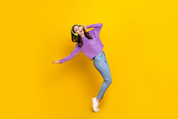 Full length profile portrait of positive pretty person standing tiptoe arm touch headphones isolated on yellow color background