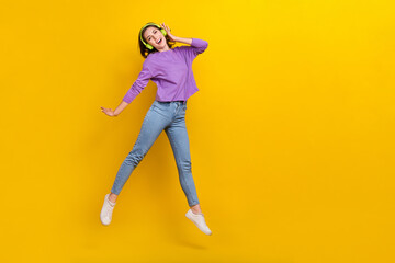 Fototapeta na wymiar Full length portrait of overjoyed crazy person jumping arm touch headphones empty space isolated on yellow color background