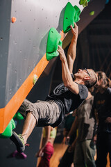 A young, athletic guy with a beautiful inflated body climbs a bouldering in a climbing hall. Emotions on the face.