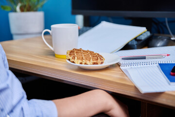 Female teenager sits at home at table studying, snacking on waffles, drinking tea