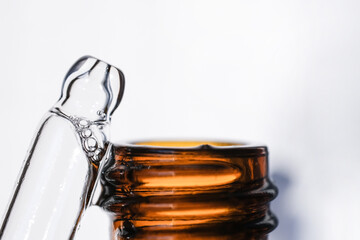 A glass pipette and amber glass bottle on a white background. Side view, macro photography, space for text.