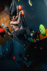 A young, athletic guy with a beautiful inflated body climbs a bouldering in a climbing hall. Emotions on the face.