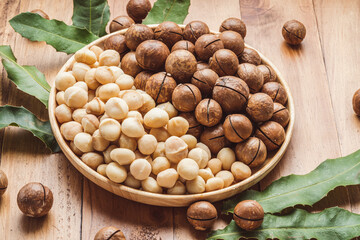 Macadamia nuts with leaf and Macadamia with hard shell on wooden plate on wooden background.