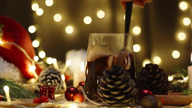 I stir marshmallows in cocoa, hot chocolate on the background of a garland of lights. Christmas table with candles and decorations. Slow motion.