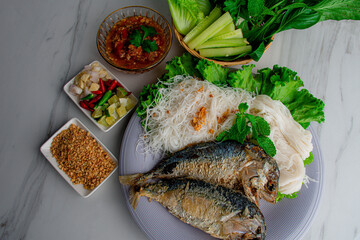 Fried two short bodied mackerel fishes and vegetable on white plate on black table 