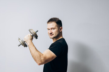 Fototapeta na wymiar Sports guy does morning exercises with dumbbells. Muscular man holds a dumbbell in one hand. Sports, health.