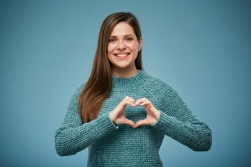 Smiling woman makes heart shaped figure with her fingers. Advertising female studio portrait on blue.