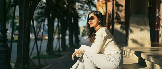 Fototapeta premium Modern millennial women in sunglasses sitting on stairs at the shopping district of a city. Banner background, panoramic view