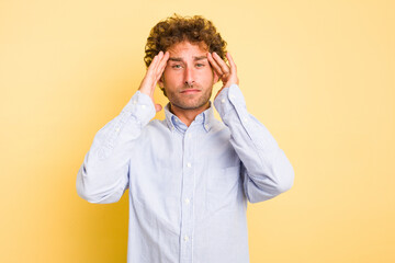 Young smart caucasian man on yellow background touching temples and having headache.
