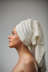 Beauty style profile portrait of young woman with bare shoulders and white towel on head. Isolated studio advertising portrait.