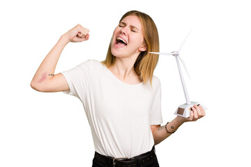 Young caucasian woman holding a small wind energy mill isolated raising fist after a victory,...
