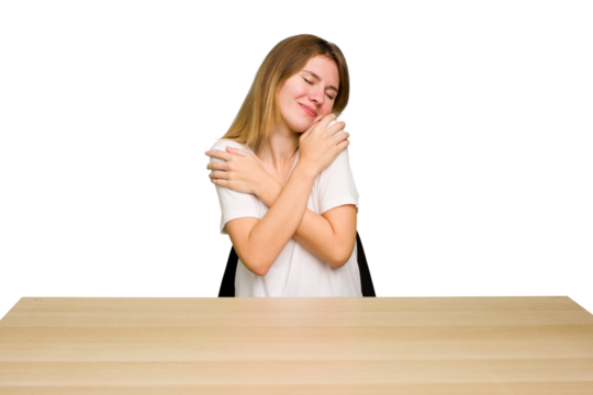 Young caucasian woman sitting on a chair in a desktop isolated hugs, smiling carefree and happy.