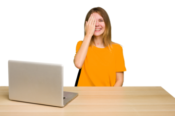 Young caucasian woman in a workplace working with a laptop isolated having fun covering half of face with palm.