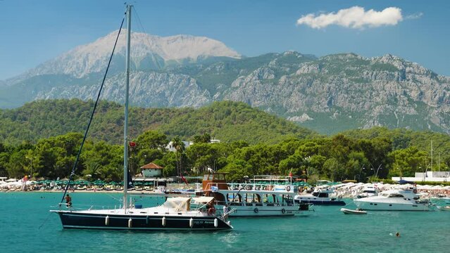 Yachts and boats stand in a beautiful lagoon on Mediterranean Sea. Beautiful landscape beach with vacationers, forest and mountains. Summer vacation at a seaside resort. Camera movement top to bottom