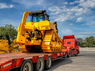 Heavy new yellow excavator on transportation truck with long trailer platform.