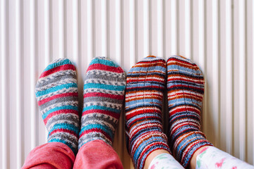 Two pairs of legs in knitted socks made of multi-colored woolen threads on heating radiator