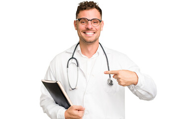 Young doctor caucasian man holding a book isolated person pointing by hand to a shirt copy space, proud and confident