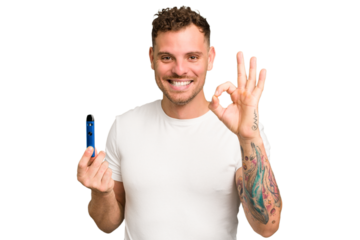 Young caucasian man holding a electronic cigarette isolated cheerful and confident showing ok gesture.
