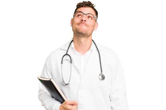 Young doctor caucasian man holding a book isolated dreaming of achieving goals and purposes