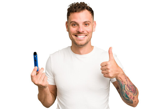 Young caucasian man holding a electronic cigarette isolated smiling and raising thumb up