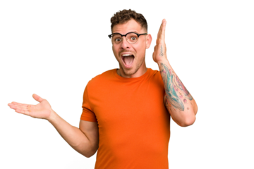 Young caucasian handsome man isolated holds copy space on a palm, keep hand over cheek. Amazed and delighted.