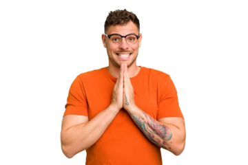 Young caucasian handsome man isolated holding hands in pray near mouth, feels confident.